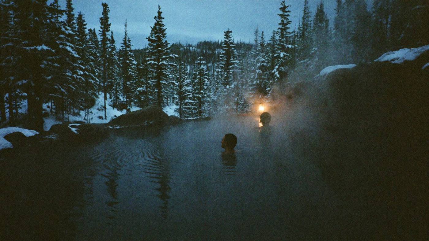 Cinematic hot spring steaming in a snowy forest at dusk